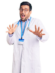 Young hispanic man wearing doctor uniform and stethoscope afraid and terrified with fear expression stop gesture with hands, shouting in shock. panic concept.