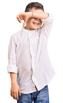 Cute blond kid wearing elegant shirt covering eyes with arm smiling cheerful and funny. blind concept.