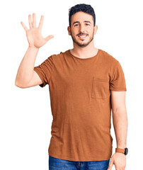 Naklejka premium Young hispanic man wearing casual clothes showing and pointing up with fingers number five while smiling confident and happy.