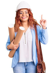 Young latin woman wearing architect hardhat holding blueprints surprised with an idea or question pointing finger with happy face, number one