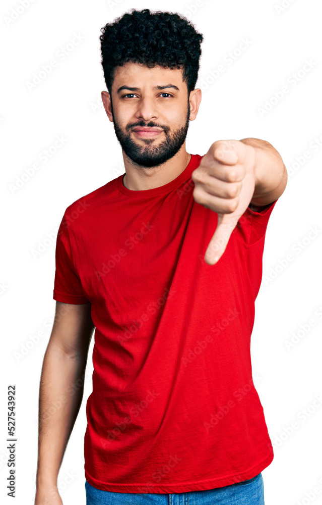 Poster Young arab man with beard wearing casual red t shirt looking unhappy and angry showing rejection and negative with thumbs down gesture. bad expression.