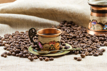 Traditional painted copper cup of coffee with heap of roasted coffee beans on sackcloth
