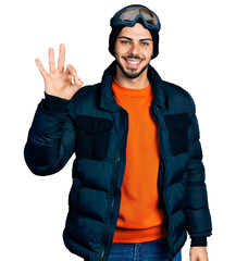 Young hispanic man with beard wearing snow wear and sky glasses smiling positive doing ok sign with hand and fingers. successful expression.