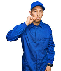 Bald man with beard wearing builder jumpsuit uniform mouth and lips shut as zip with fingers....