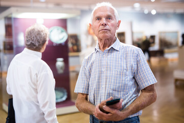 mature European man examines paintings in an exhibition in hall of an art museum