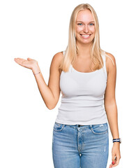 Fototapeta premium Young blonde girl wearing casual style with sleeveless shirt smiling cheerful presenting and pointing with palm of hand looking at the camera.