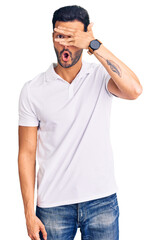 Fototapeta premium Young handsome hispanic man wearing casual clothes peeking in shock covering face and eyes with hand, looking through fingers with embarrassed expression.