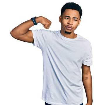Young african american man wearing casual white t shirt strong person showing arm muscle, confident and proud of power