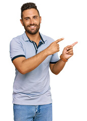 Handsome man with beard wearing casual clothes smiling and looking at the camera pointing with two hands and fingers to the side.