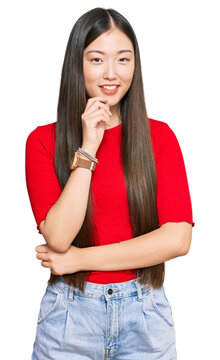 Young chinese woman wearing casual clothes looking confident at the camera with smile with crossed arms and hand raised on chin. thinking positive.