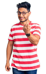 Handsome latin american young man wearing casual clothes and glasses beckoning come here gesture with hand inviting welcoming happy and smiling