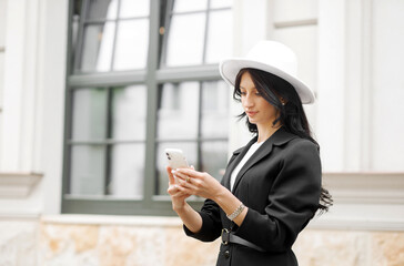 Business woman looking on smart phone. Caucasian female in white hat standing outside.