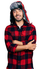 Hispanic young man with beard wearing fluffy earmuff hat happy face smiling with crossed arms looking at the camera. positive person.