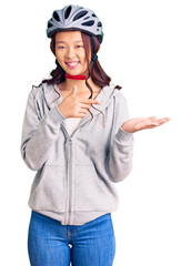 Young beautiful chinese girl wearing bike helmet amazed and smiling to the camera while presenting with hand and pointing with finger.