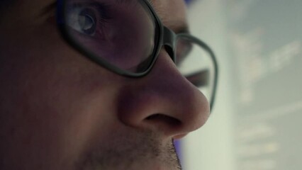 A programmer, a man in front of a computer, the code is reflected in the glasses. Working in IT, learning programming languages, developing applications and software.