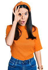 Young hispanic woman wearing casual clothes doing ok gesture shocked with surprised face, eye looking through fingers. unbelieving expression.