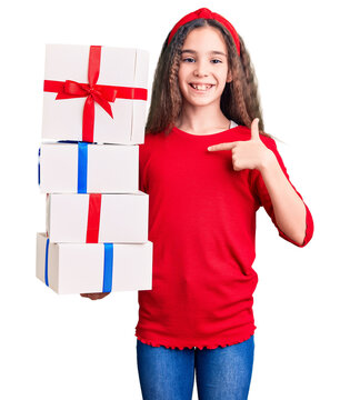Cute hispanic child girl holding gift pointing finger to one self smiling happy and proud
