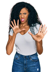 Middle age african american woman wearing casual white t shirt afraid and terrified with fear expression stop gesture with hands, shouting in shock. panic concept.