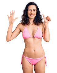 Young beautiful hispanic woman wearing bikini showing and pointing up with fingers number six while smiling confident and happy.