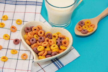 children's dry breakfast multicolored rings in a plate and a wooden spoon, next to a white milk drink in a transparent mug