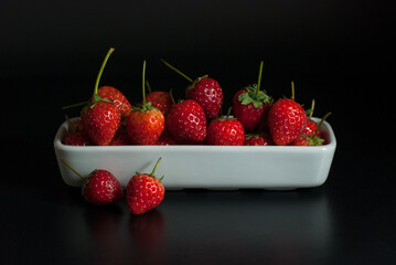 Several strawberries are housed in white ceramic vessels and placed on a black background.