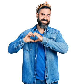Hispanic man with beard wearing king crown smiling in love showing heart symbol and shape with hands. romantic concept.