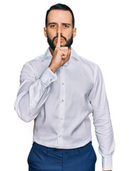 Young man with beard wearing business shirt asking to be quiet with finger on lips. silence and...