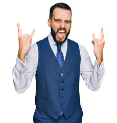 Young man with beard wearing business vest shouting with crazy expression doing rock symbol with hands up. music star. heavy concept.
