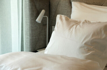Close-up fragment of bedroom with Soft pillow and blanket, stylish white reading lamp in cozy modern interior​ design home or hotel. Stylish comfortable furniture. Selective focus.