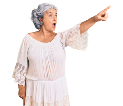 Senior woman with gray hair wearing bohemian style pointing with finger surprised ahead, open mouth amazed expression, something on the front