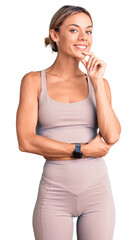 Beautiful caucasian woman wearing sportswear looking confident at the camera smiling with crossed arms and hand raised on chin. thinking positive.