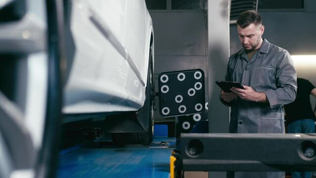 A car service employee installs a wheel adapter with a target on the wheel to perform a wheel alignment. Diagnostics and balancing of wheels of a lifting trolley at a modern service station.