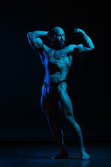 Fototapeta na wymiar Athletic man demonstrates muscles in the light of a blue light filter on a dark background.