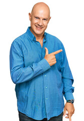Middle age bald man wearing casual clothes cheerful with a smile on face pointing with hand and finger up to the side with happy and natural expression
