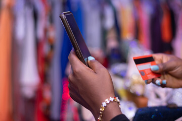 african lady using phone and credit card in a shop to pay