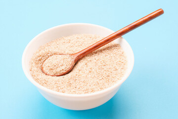 Wooden spoon in a bowl with psyllium husk close-up on blue background.