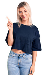 Young beautiful blonde woman wearing casual t-shirt showing and pointing up with finger number one while smiling confident and happy.