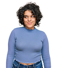 Young hispanic woman with curly hair wearing casual clothes smiling looking to the side and staring away thinking.