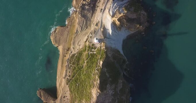 Directly above Castlepoint lighthouse in New Zealand, moving along the ridgeline of a cliff towards a rocky bay and beach.