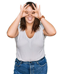 Obraz na płótnie Canvas Young plus size woman wearing casual white t shirt doing ok gesture like binoculars sticking tongue out, eyes looking through fingers. crazy expression.