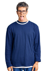 Young handsome man wearing casual clothes and glasses sticking tongue out happy with funny expression. emotion concept.