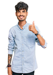 Young hispanic man wearing casual clothes doing happy thumbs up gesture with hand. approving expression looking at the camera showing success.