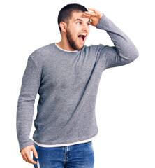 Young handsome man wearing casual sweater very happy and smiling looking far away with hand over head. searching concept.