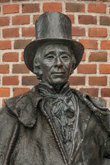 bronse statue of th danish author H C Andersen in a top hat in front of a red brickwall
