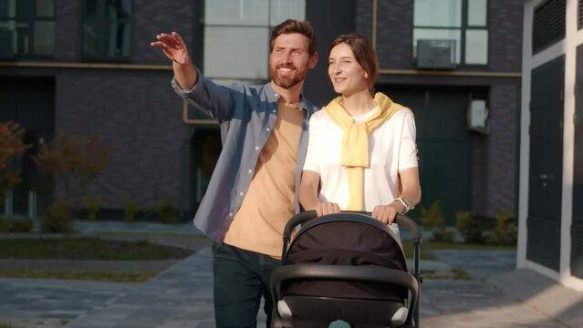 Cute shot of a young family husband and wife walking with a newborn baby in a stroller in the sunlight on street. Feel happy smiling. Parenthood. Slow motion