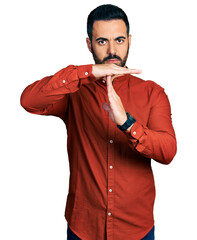 Young hispanic man with beard wearing casual shirt doing time out gesture with hands, frustrated...