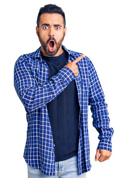 Young hispanic man wearing casual clothes surprised pointing with finger to the side, open mouth amazed expression.