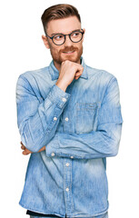 Young redhead man wearing casual denim shirt with hand on chin thinking about question, pensive expression. smiling with thoughtful face. doubt concept.