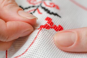 Naklejka premium Close-up of female hands cross stitching on a white canvas. A woman embroiders the national symbols of Ukraine with a cross.