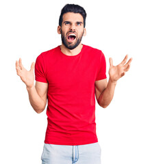 Young handsome man with beard wearing casual t-shirt crazy and mad shouting and yelling with aggressive expression and arms raised. frustration concept.